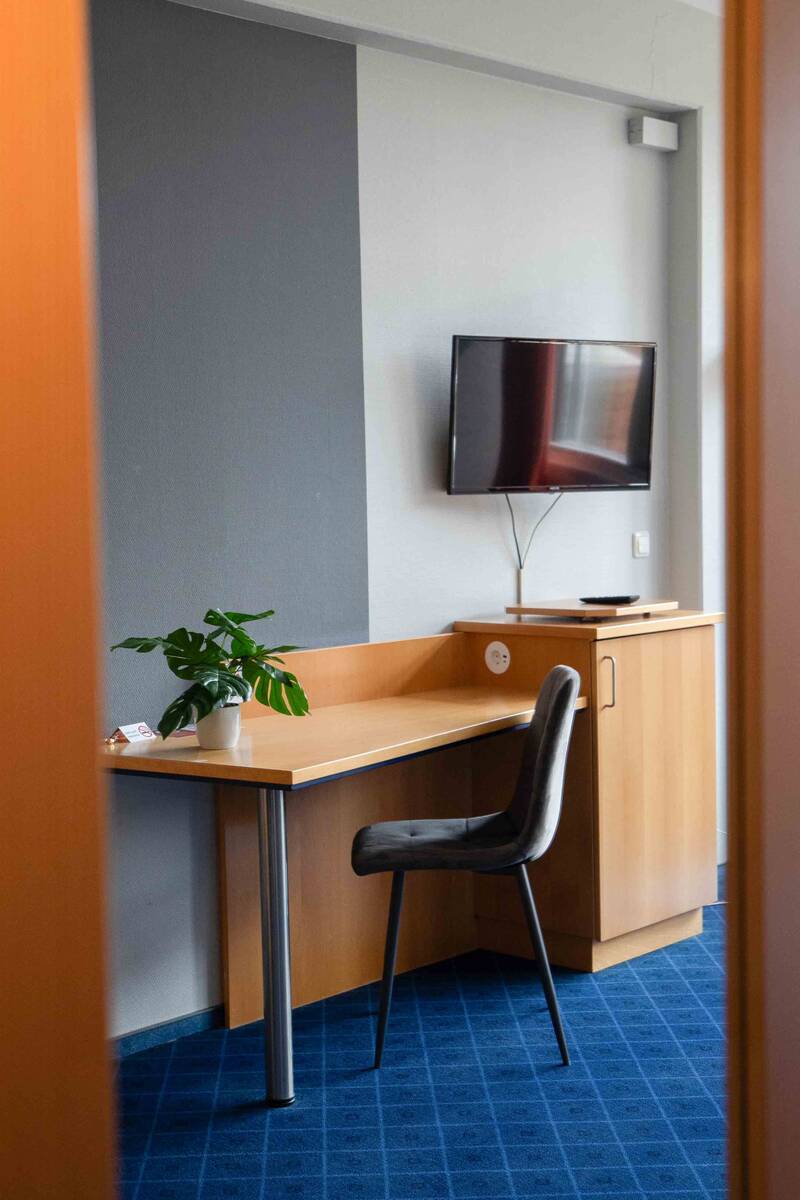 Großzügiger Arbeitsbereich in einem Hotelzimmer mit Holzschreibtisch, schwarzem Stuhl und Flachbildfernseher an der Wand.