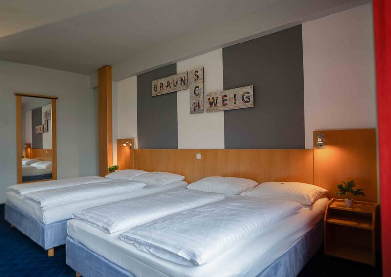 Riesiges Hotelzimmer mit zwei 160cm breiten Doppelbetten vor einer modernen grauen Wand.